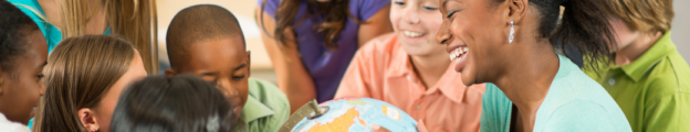 Black female teacher holds a globe and smiles as a diverse group of elementary students gather round engaged.