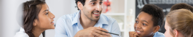 Smiling Indian male teacher talks with a group of diverse middle school students.