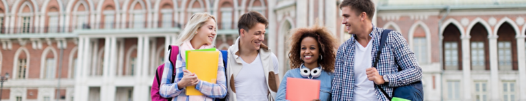 Four diverse high school students smiling and walking side by side as a group with a college building behind them.