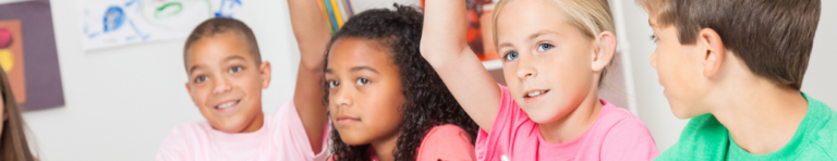 Diverse group of elementary students raise their hands to answer a question.