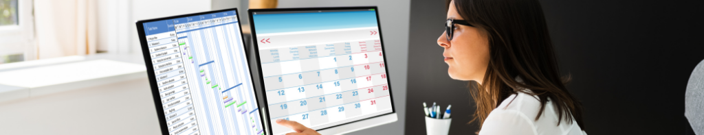Professional woman in glasses points to two computer screens depicting a calendar and schedule.