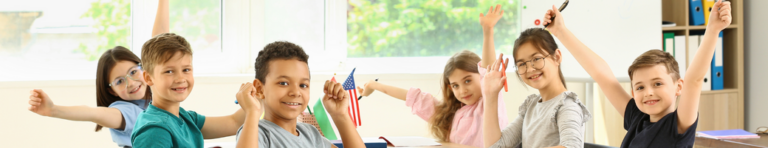 Diverse group of elementary students sit in a circle, smiling and waving their hands in the air.