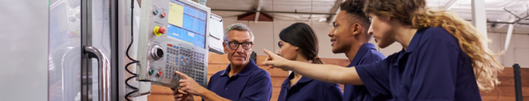 Mature male auto-mechanics teacher answering questions about a machine from three diverse high school students, one is pointing at the machine.