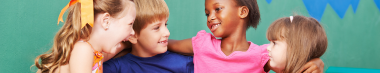 Diverse group of four elementary students have their arms linked behind each other's shoulders in comfort and solidarity.