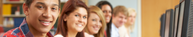 Diverse group of smiling high school students sitting in front of a row of computers.