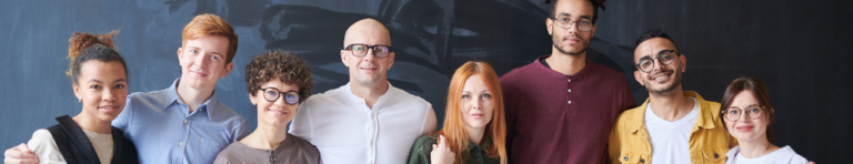 Diverse group of people stand in front of a blackboard smiling.