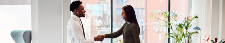 A Black man in white button-up shirt and black tie shakes hands with professional Indian woman in a dark green sweater.